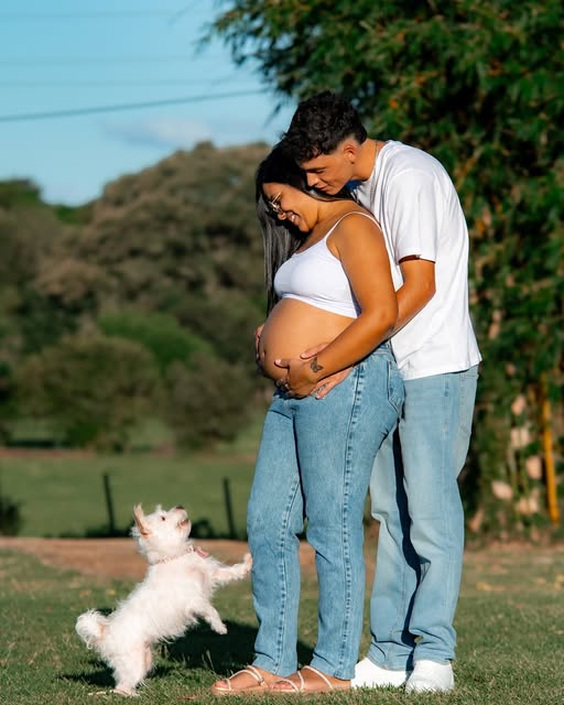 Pareja abrazada en una sesión de embarazo al aire libre, con su perro