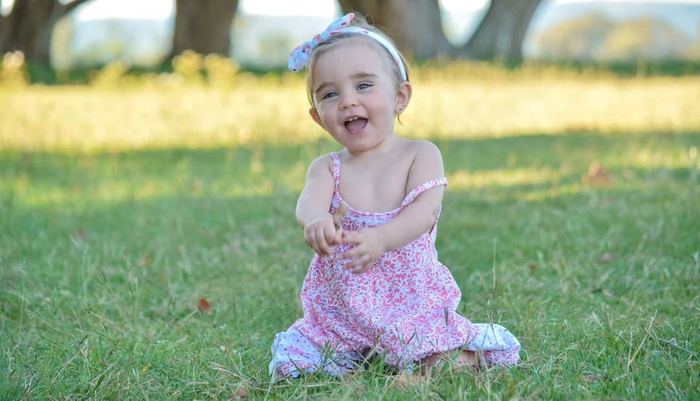 Bebé sentada en el pasto con vestido rosa
