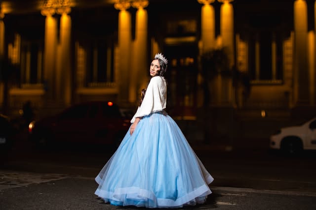 Quinceañera con vestido celeste frente a un edificio iluminado de noche