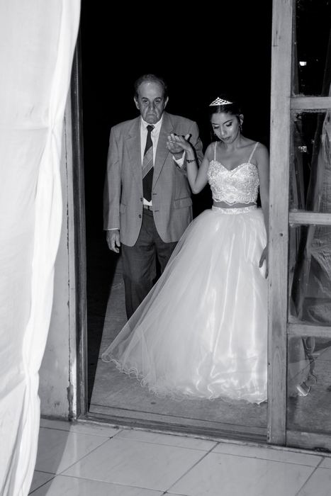 Quinceañera entrando al salón del brazo de su padre, en blanco y negro